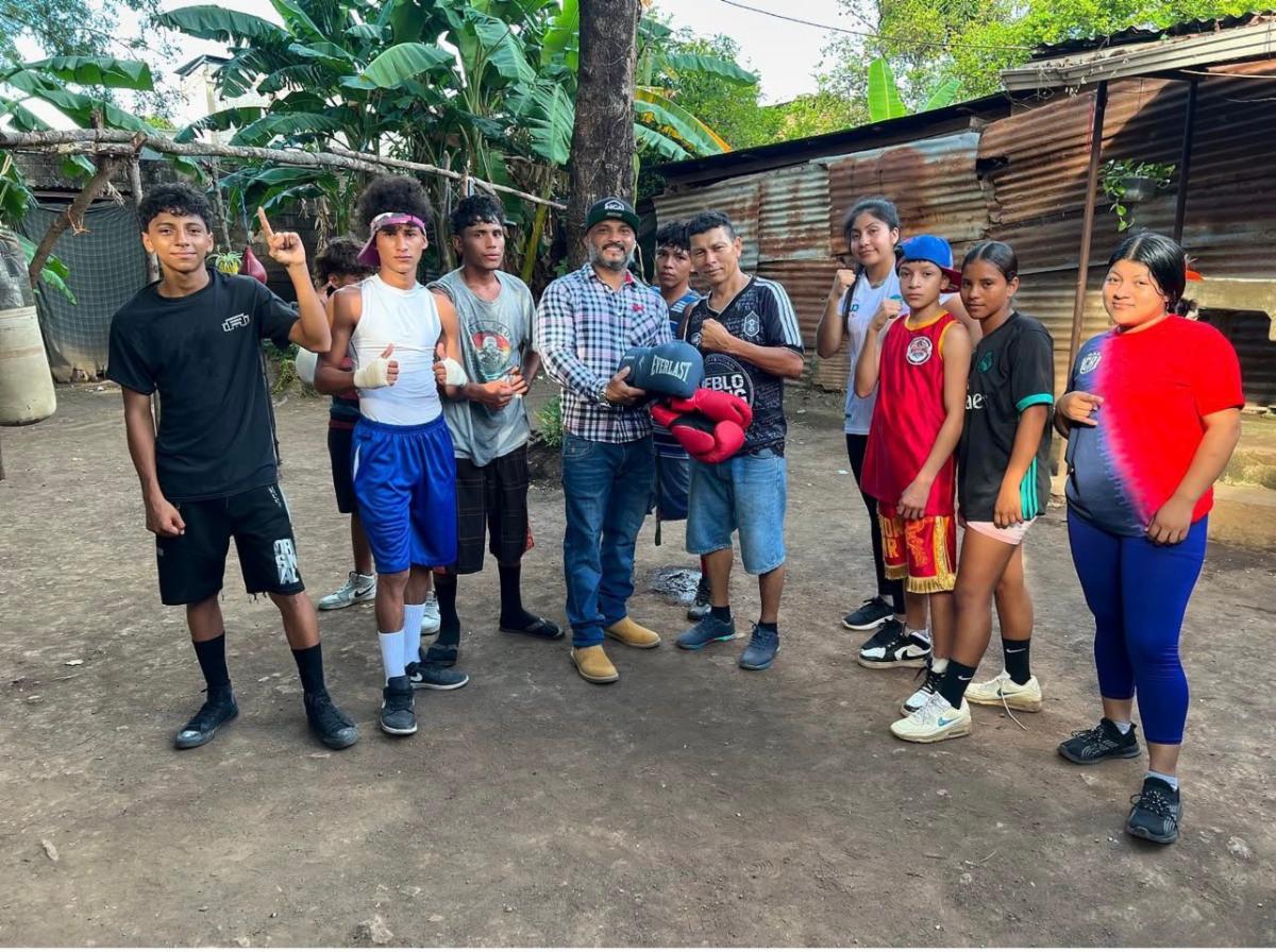 Boxing 5 - Neighbors to Nicaragua Group of young boxers and two coaches posing outdoors with boxing gloves and punch mitts in a yard.