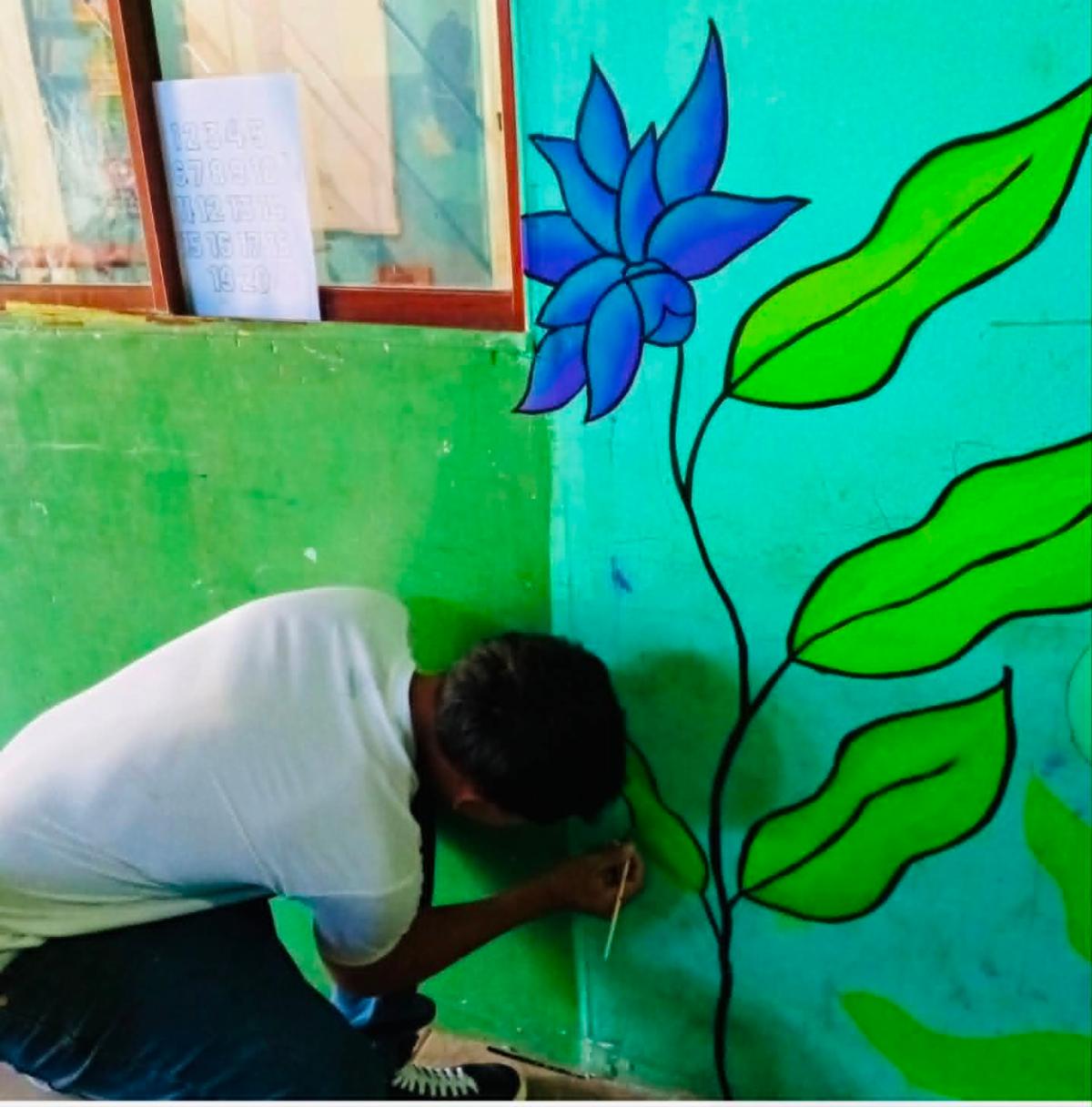 Candid2 - Neighbors to Nicaragua Person kneeling and painting a large blue flower with green leaves on a turquoise wall mural.
