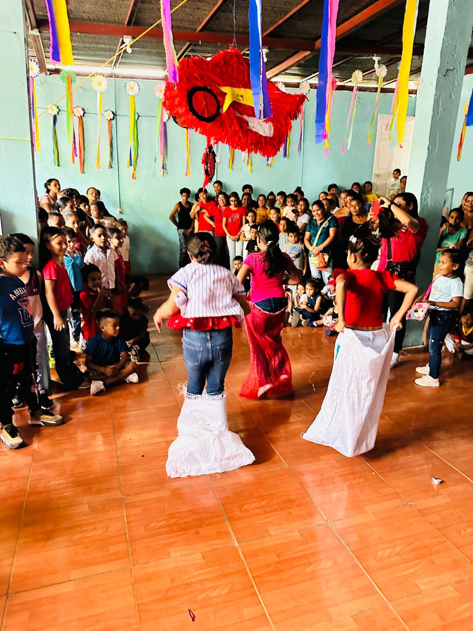 MothersDay7 - Neighbors to Nicaragua Children and adults gathered in a decorated room watching dancers perform in the center beneath a large red dragon decoration and colorful streamers.