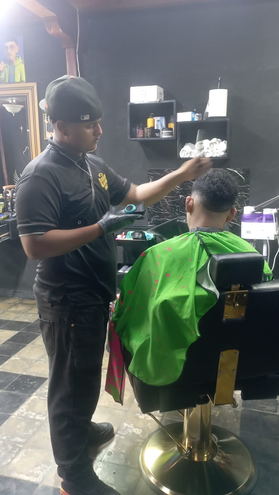 Ramon2 - Neighbors to Nicaragua Barber in a black uniform cutting a customer's hair with a green cape in a classic barbershop setting