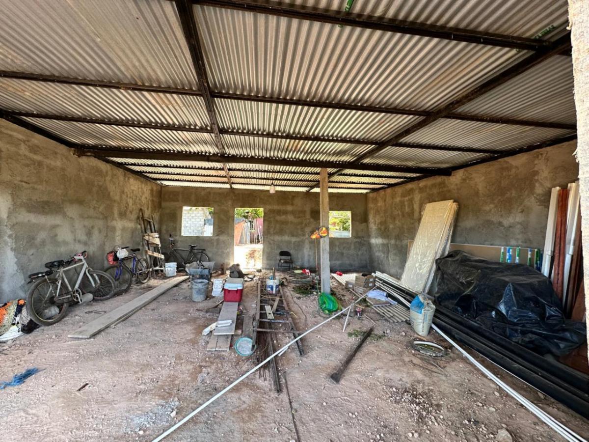Interior of a cluttered unfinished workshop with bikes and assorted building materials on a dirt floor.